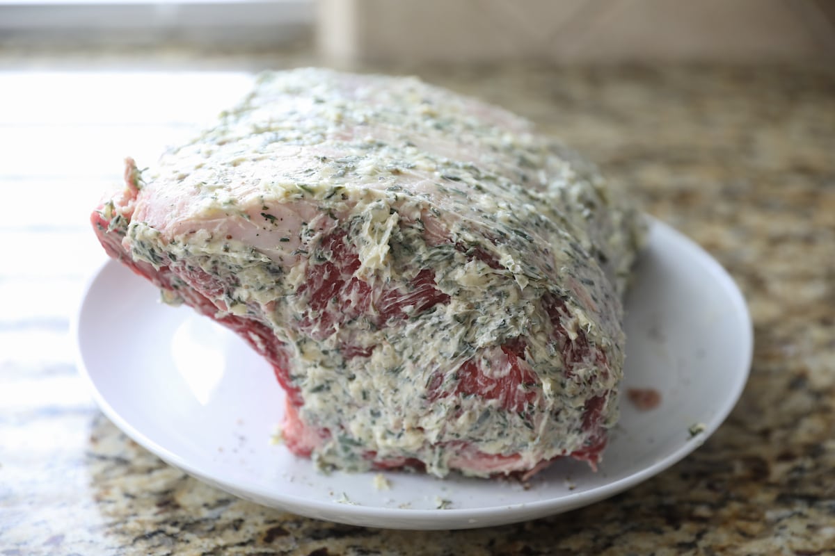whole standing rib roast covered in herb butter on white plate