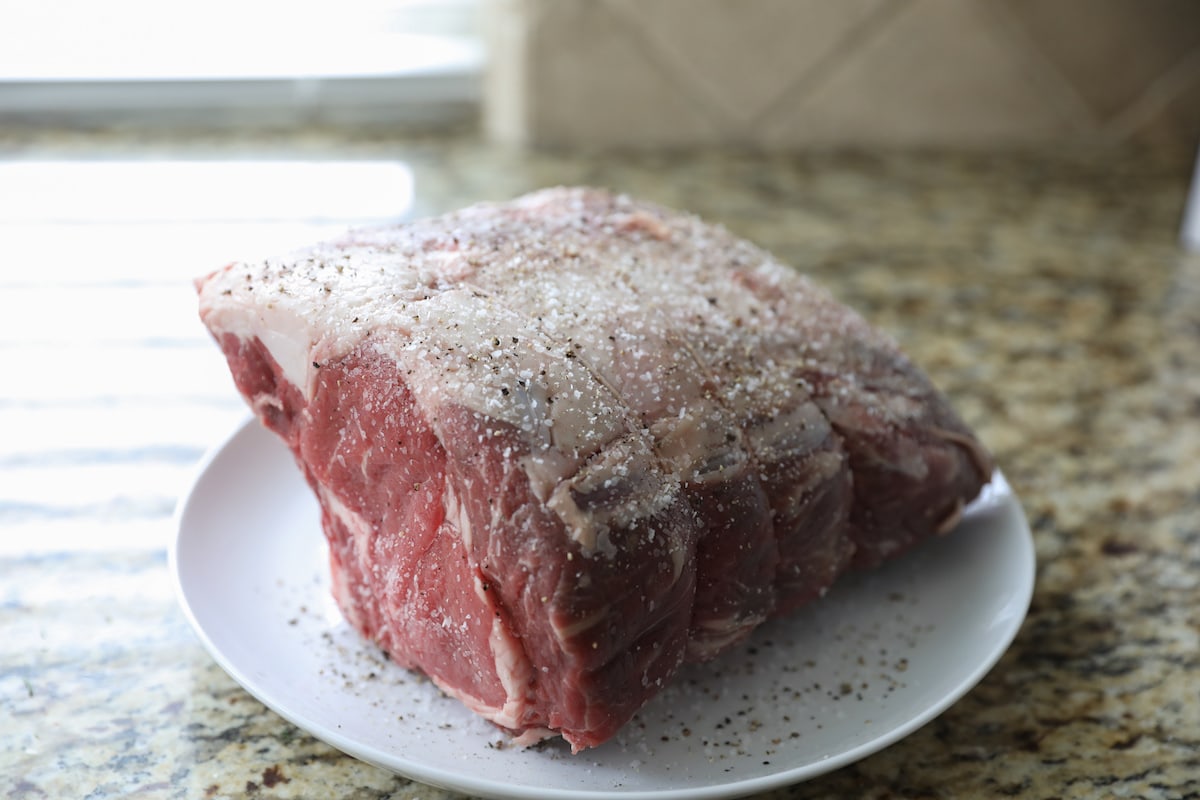 standing rib roast on white plate with salt and pepper