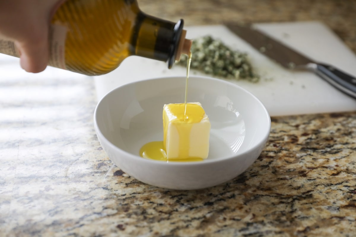 pouring olive oil over butter in small white bowl