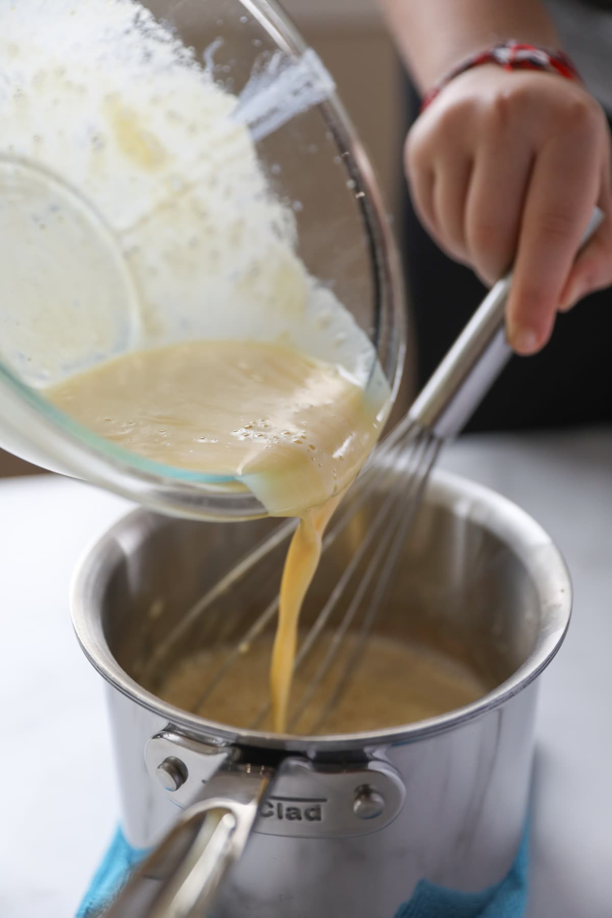 pouring tempered egg yolks into hot milk