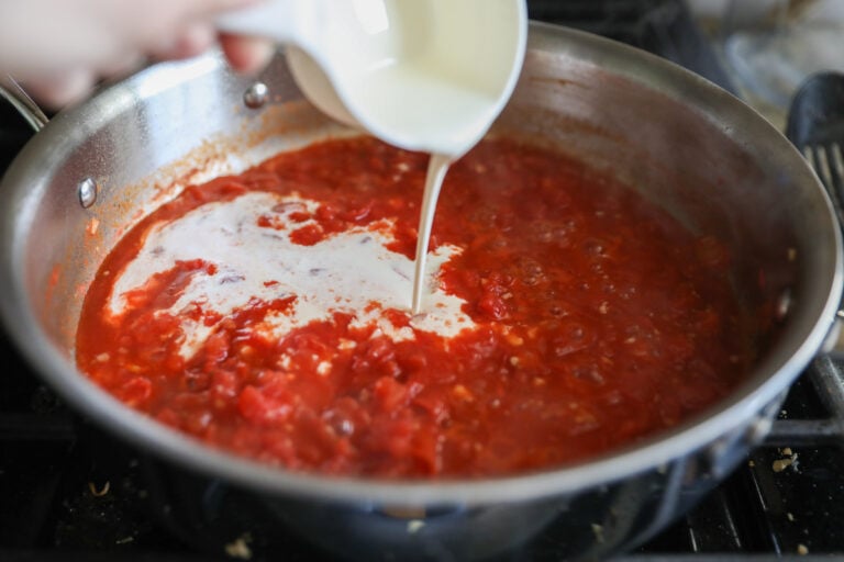 pouring heavy cream into pan with tomato sauce