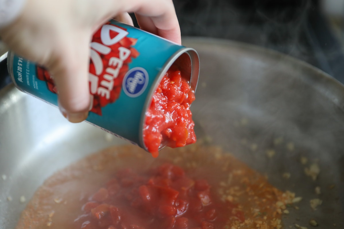 pouring diced tomatoes into hot pan