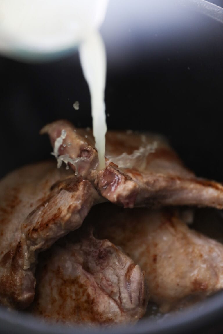 pouring chicken broth onto pork chops in instant pot