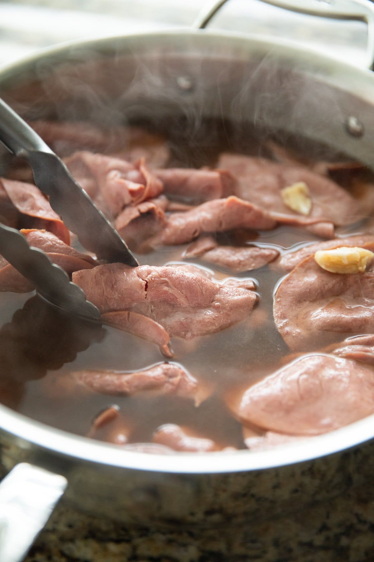 hot roast beef in au jus in pan with tongs