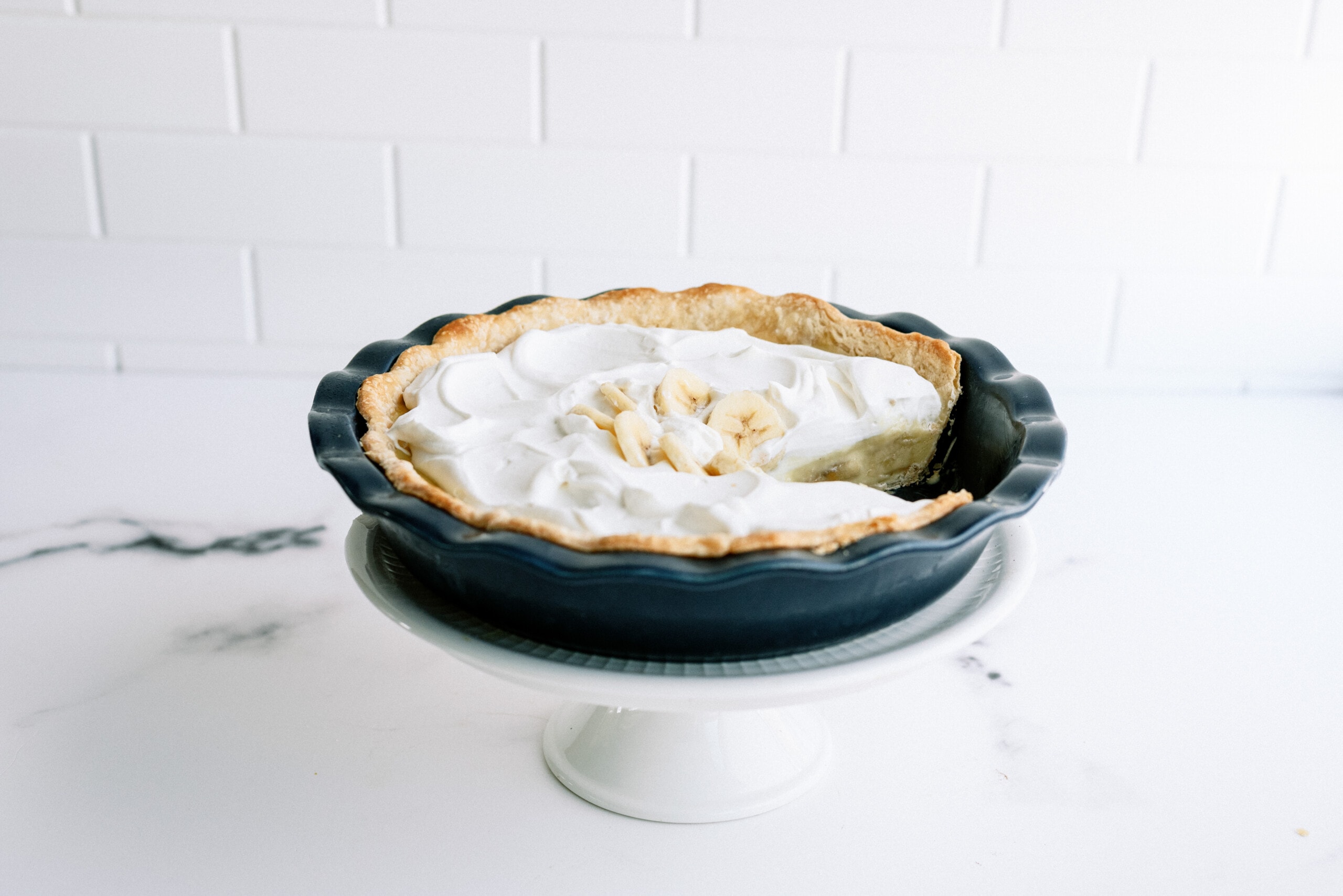 banana cream pie in a pie dish on top of a cake platter