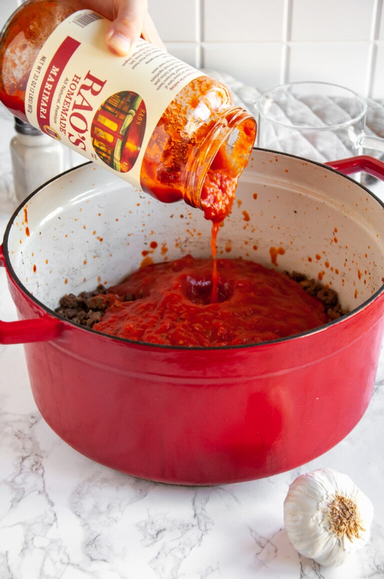 adding marinara sauce to the ground beef in the red cooking pot