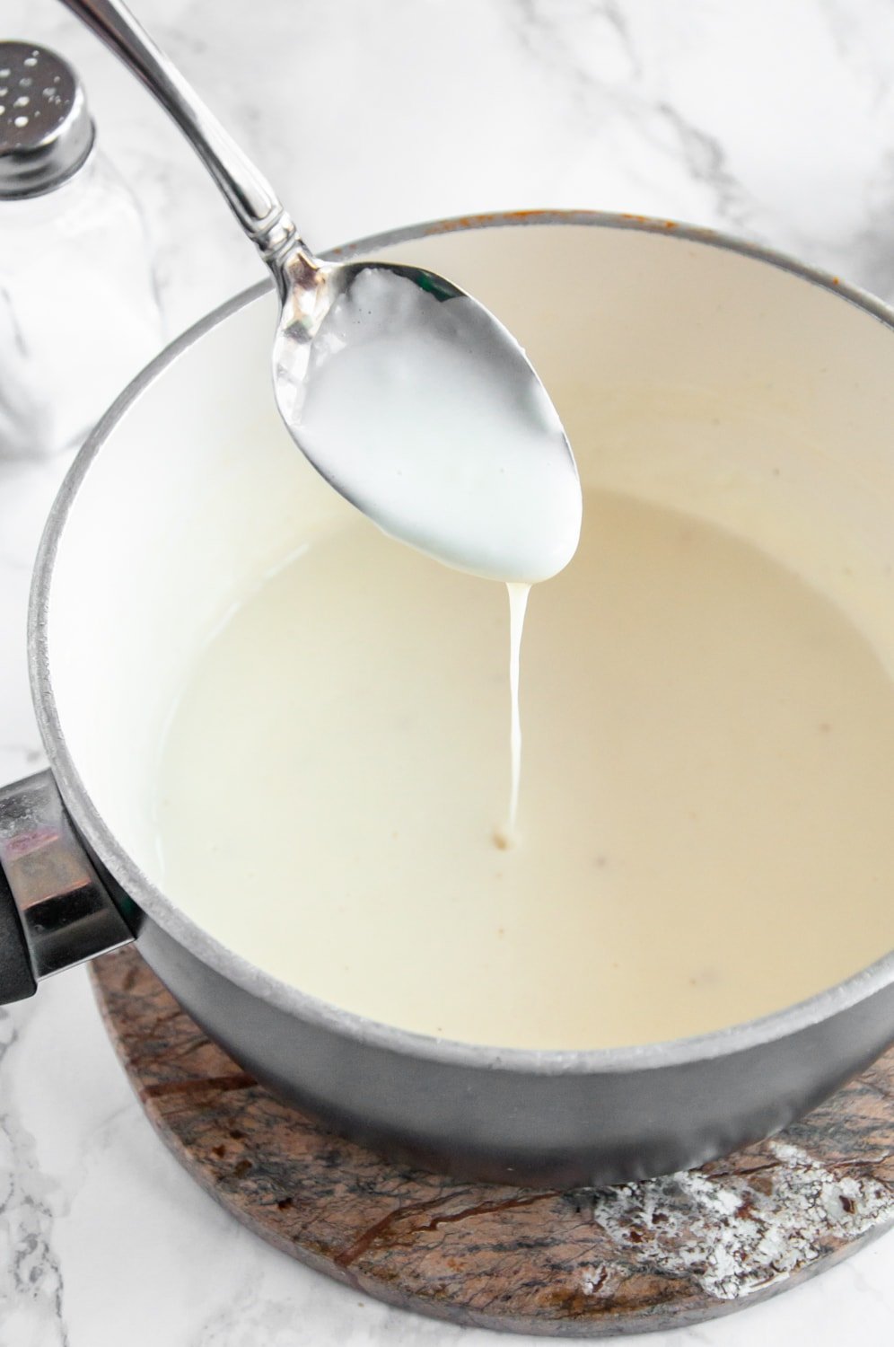 Bechamel sauce in a cooking pot with a spoon scooping some of the sauce out