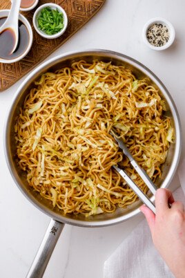 hand holding tongs into a pot of chow mein