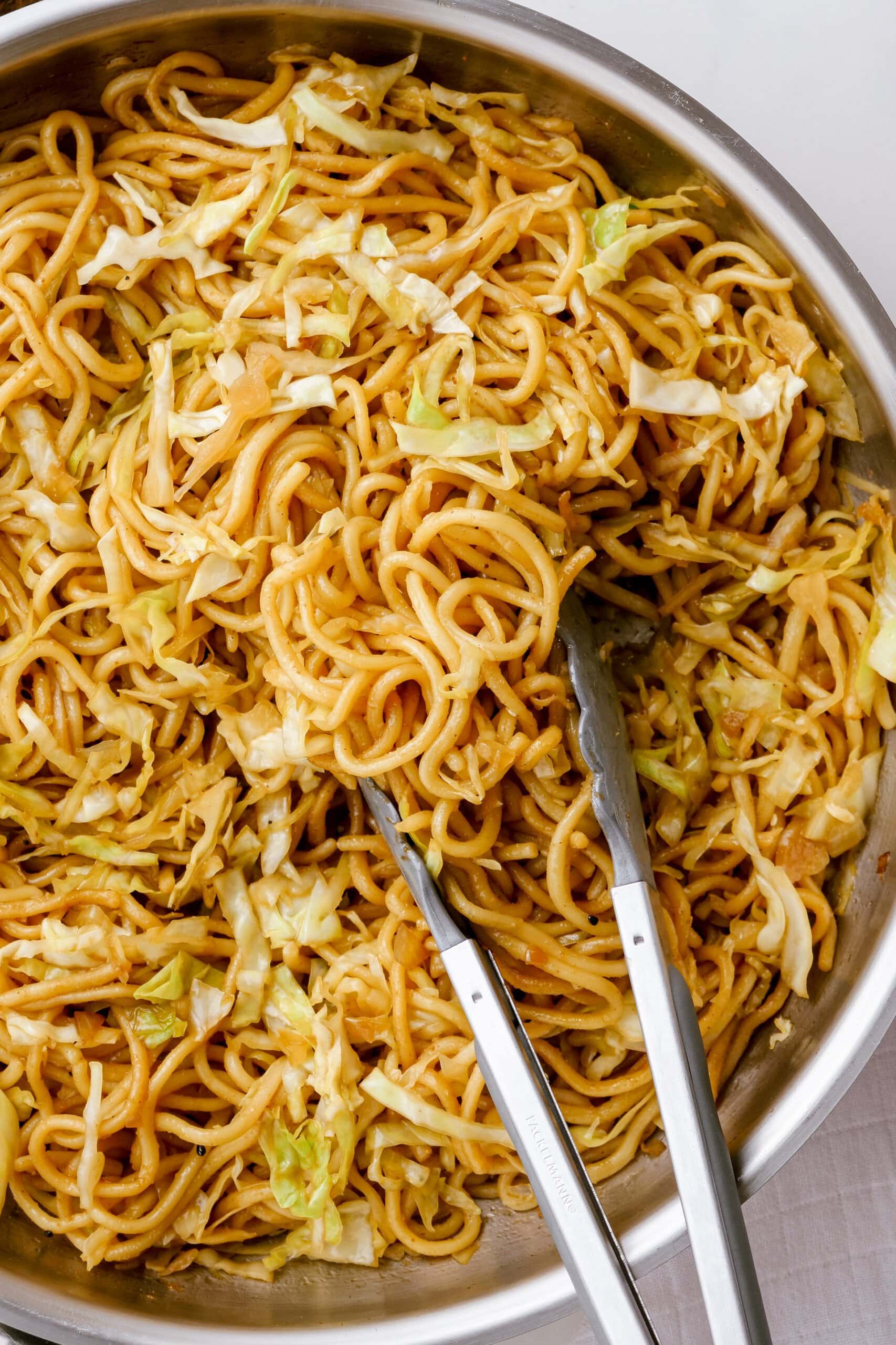 close up of tongs resting in a pot of chow mein