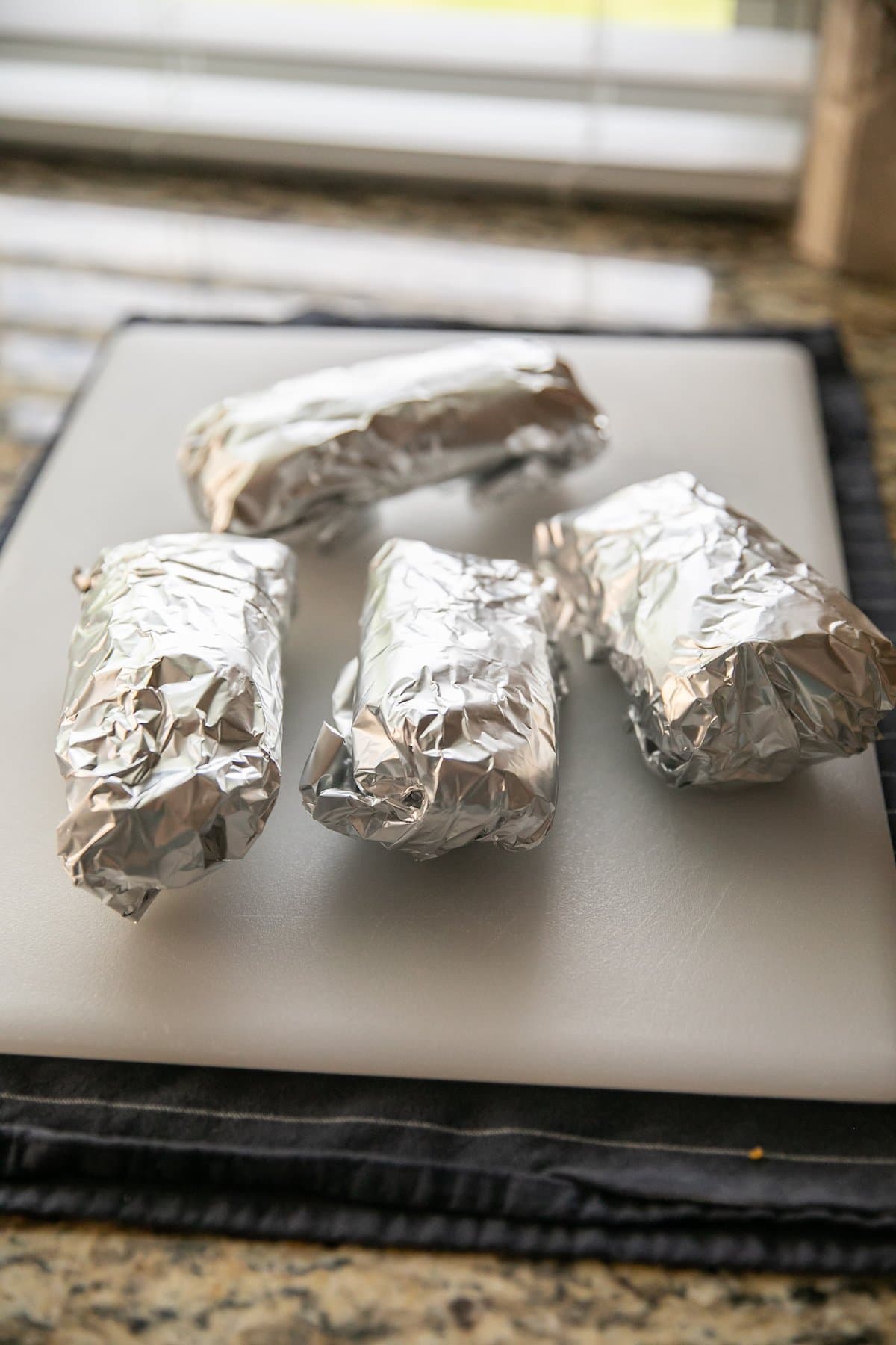 foil wrapped breakfast burritos on a cutting board