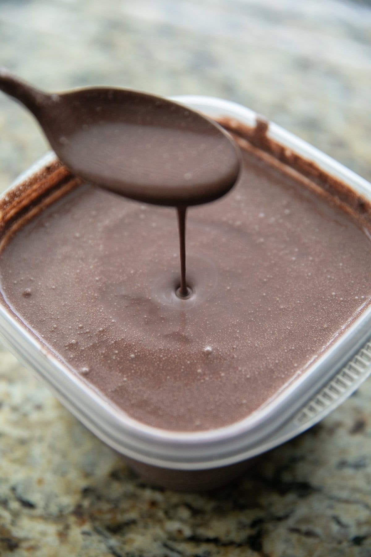 chocolate base in a plastic container with a spoon lifting some of the mixture out