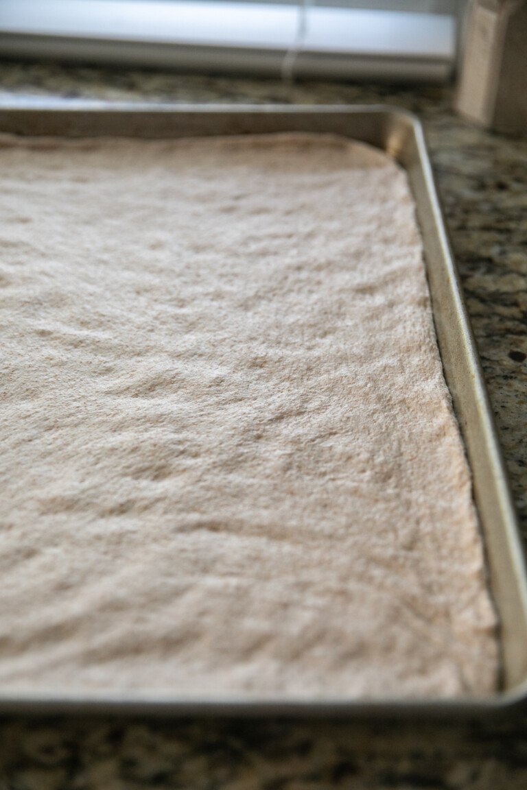 whole wheat pizza dough spread out on a baking sheet