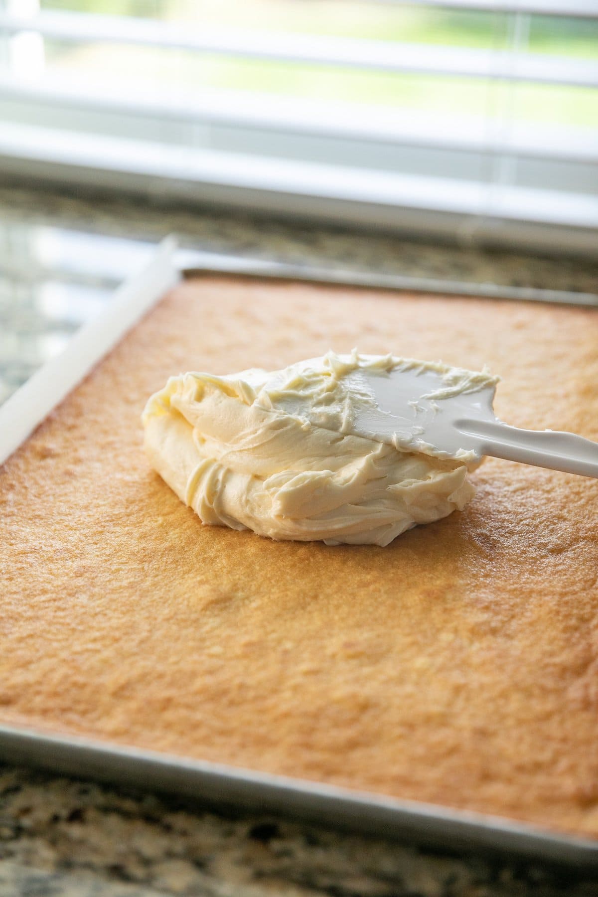 spreading frosting on cooled vanilla sheet cake