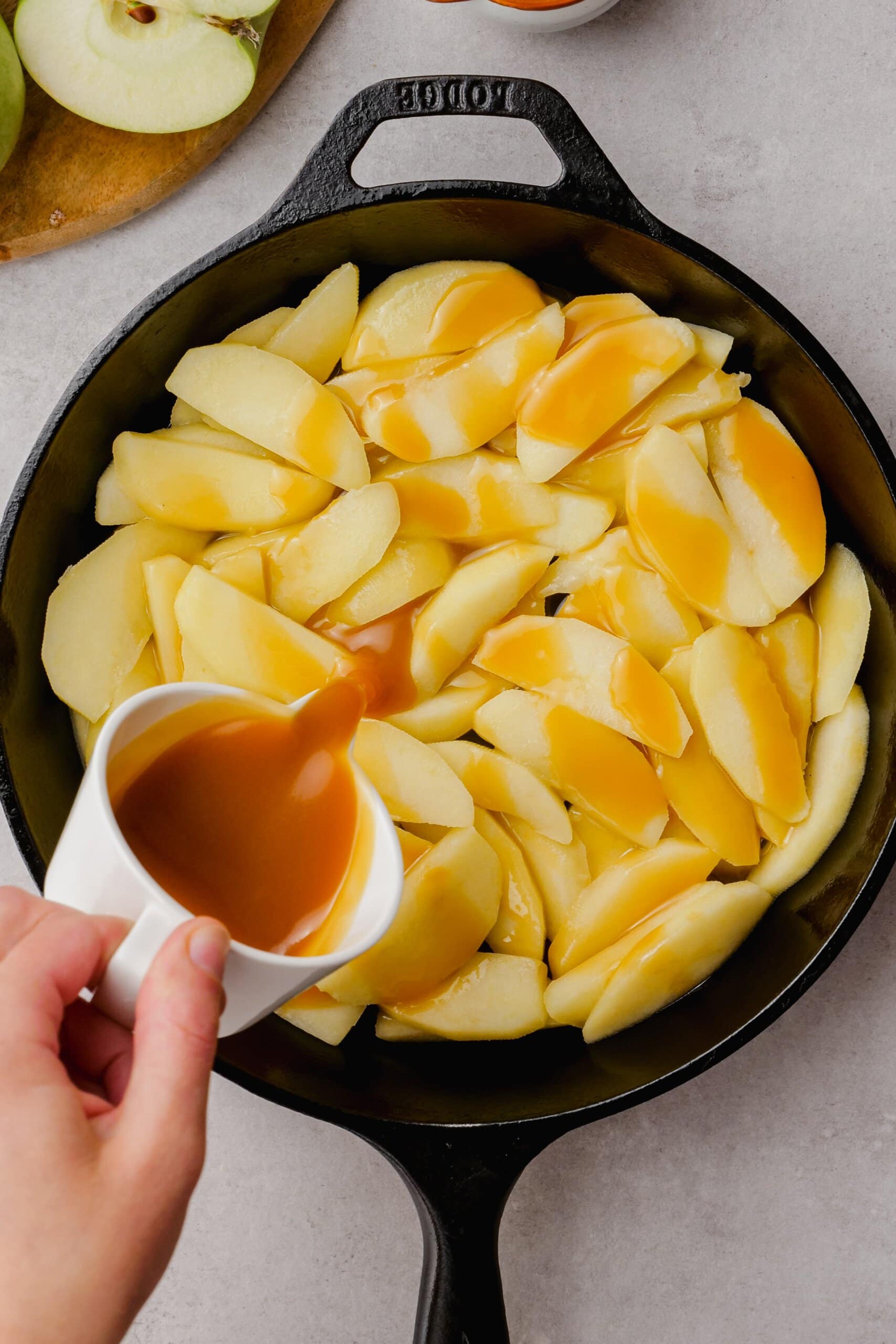 pouring salted caramel sauce over cooked apples all in a cast iron skillet