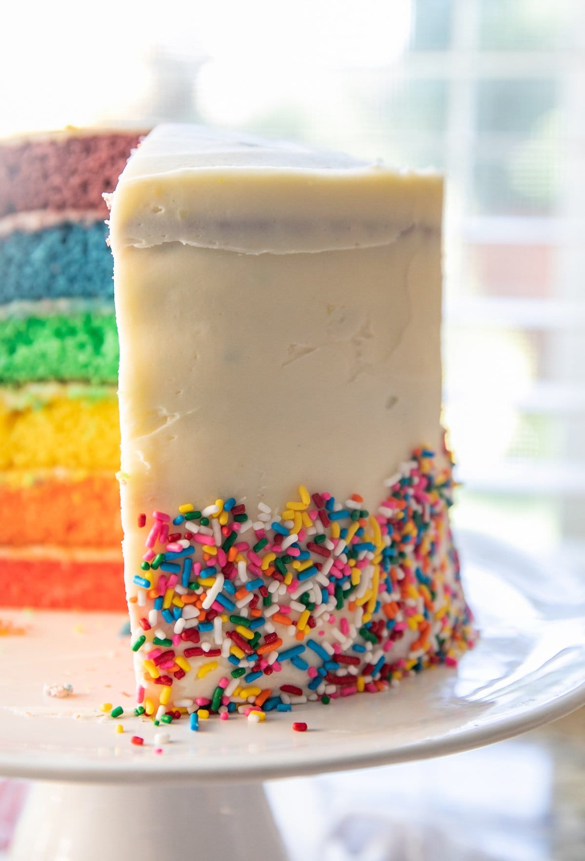 frosted rainbow cake with a slice taken out of it