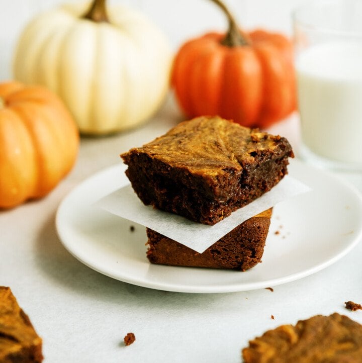 two pumpkin brownies stacked on top of each other separated by parchment paper all on a white plate