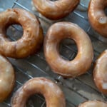 top down view of glazed donuts on a cooling wrack about a parchment paper lined baking sheet