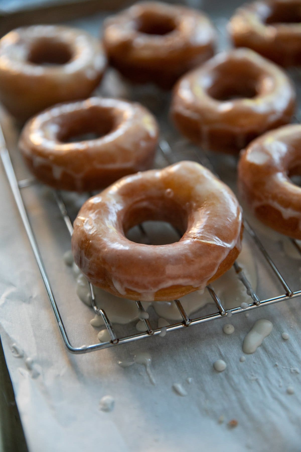 glazed donuts on a cooling wrack about a parchment paper lined baking sheet