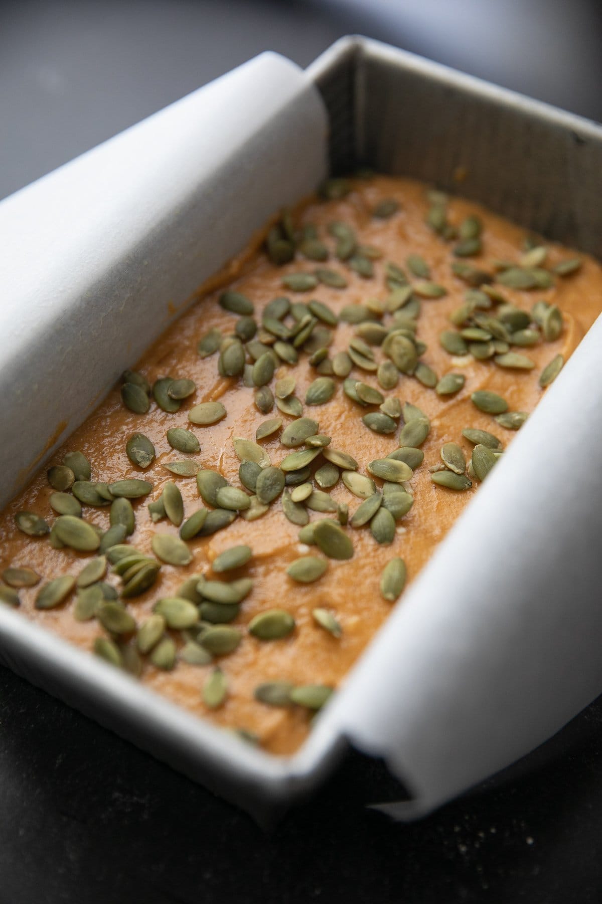 pumpkin. bread batter in a parchment paper lined loaf pan sprinkled with green pepitas