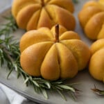 pumpkin bread rolls on a serving plate with greenery