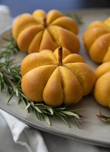 pumpkin bread rolls on a serving plate with greenery