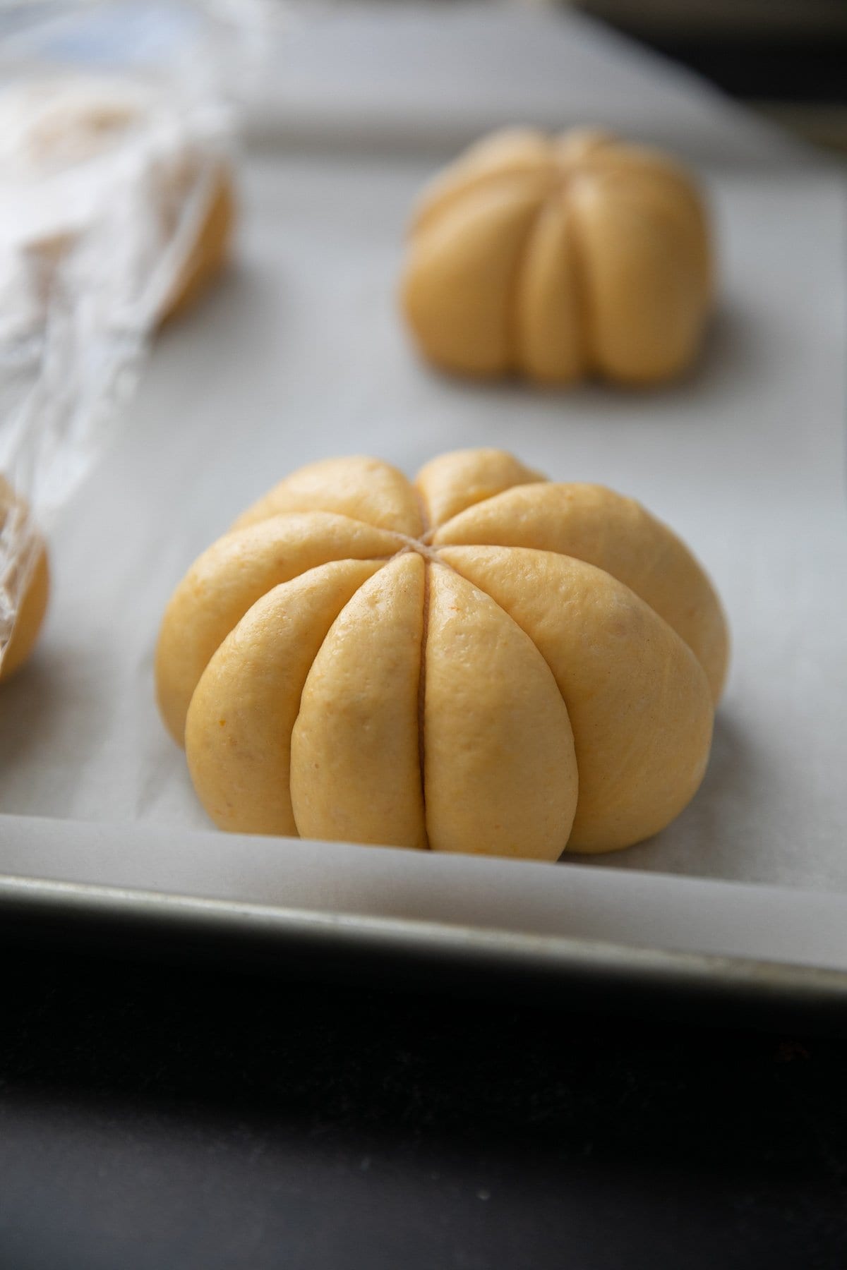 unbaked pumpkin bread rolls rising for the second time on a parchment paper lined baking sheet