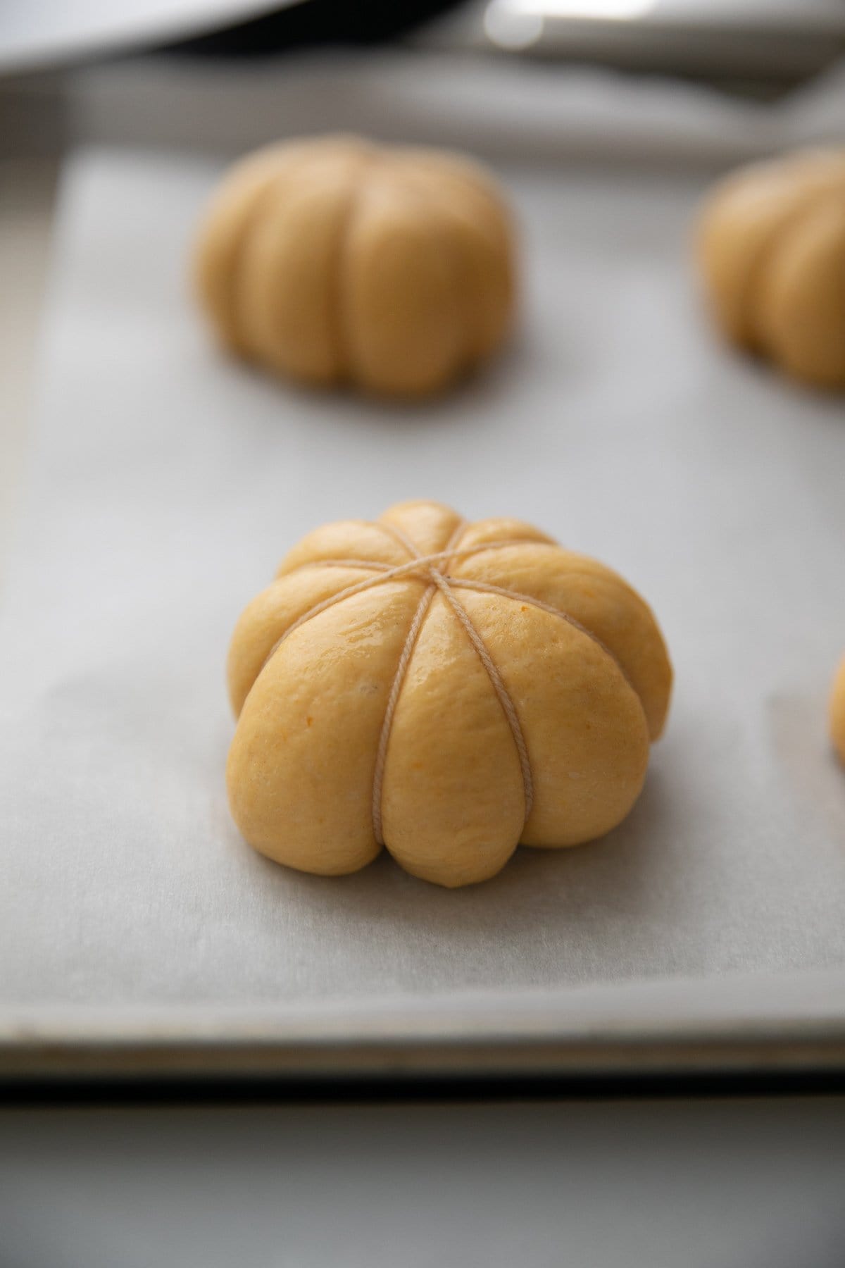 bakers string wrapped around dough ball to make it look like a pumpkin, all on a parchment paper lined baking sheet