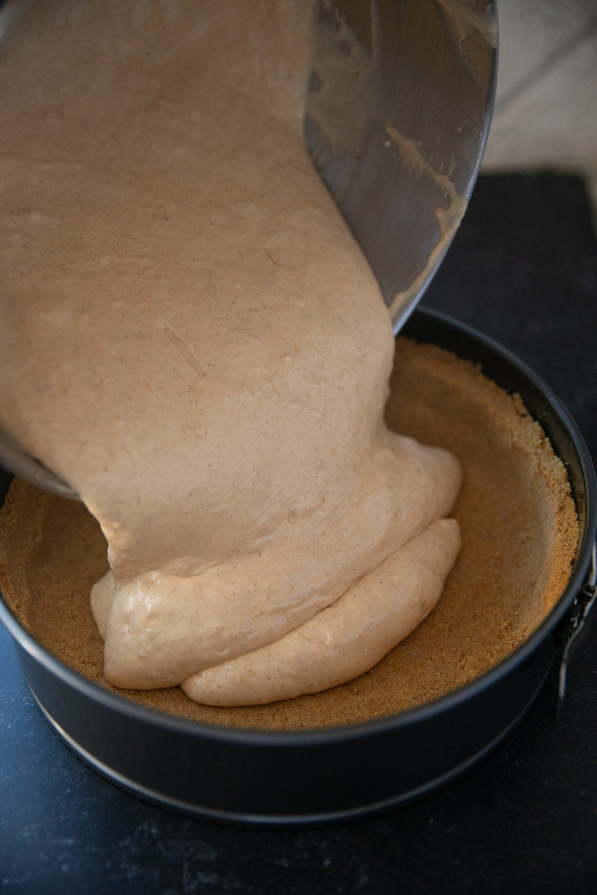 pouring pumpkin cheesecake batter into the baked graham cracker crust
