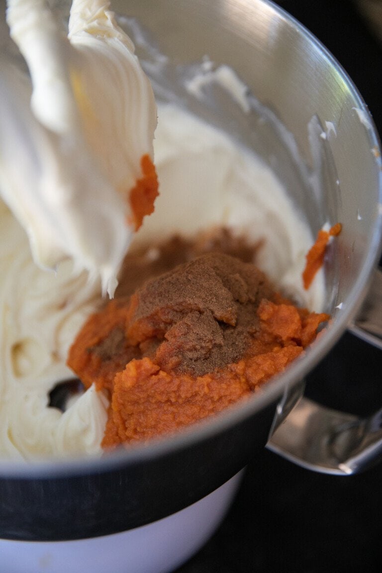adding pumpkin, flour, vanilla and spices to cream cheese mixture all in a metal bowl