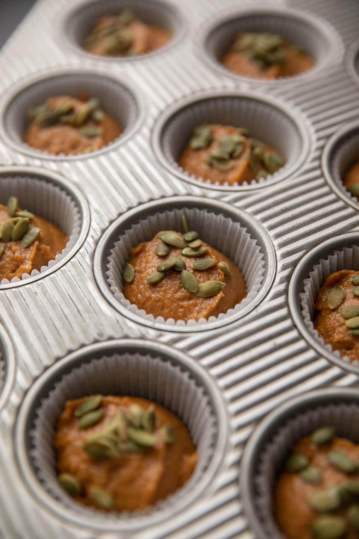pumpkin muffin batter in muffin tins topped with green pepita seeds