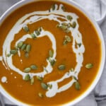 pumpkin soup in a bowl with a cream swirl and topped with pepitas