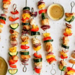 honey-soy-chicken-kabobs on oval white background with bowl of sauce