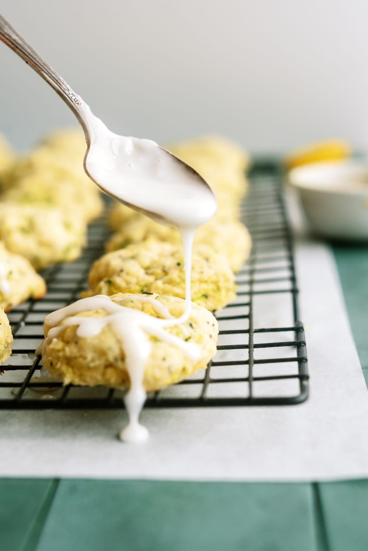 lemon-zucchini-cookies on cooling rack being glazed with spoon