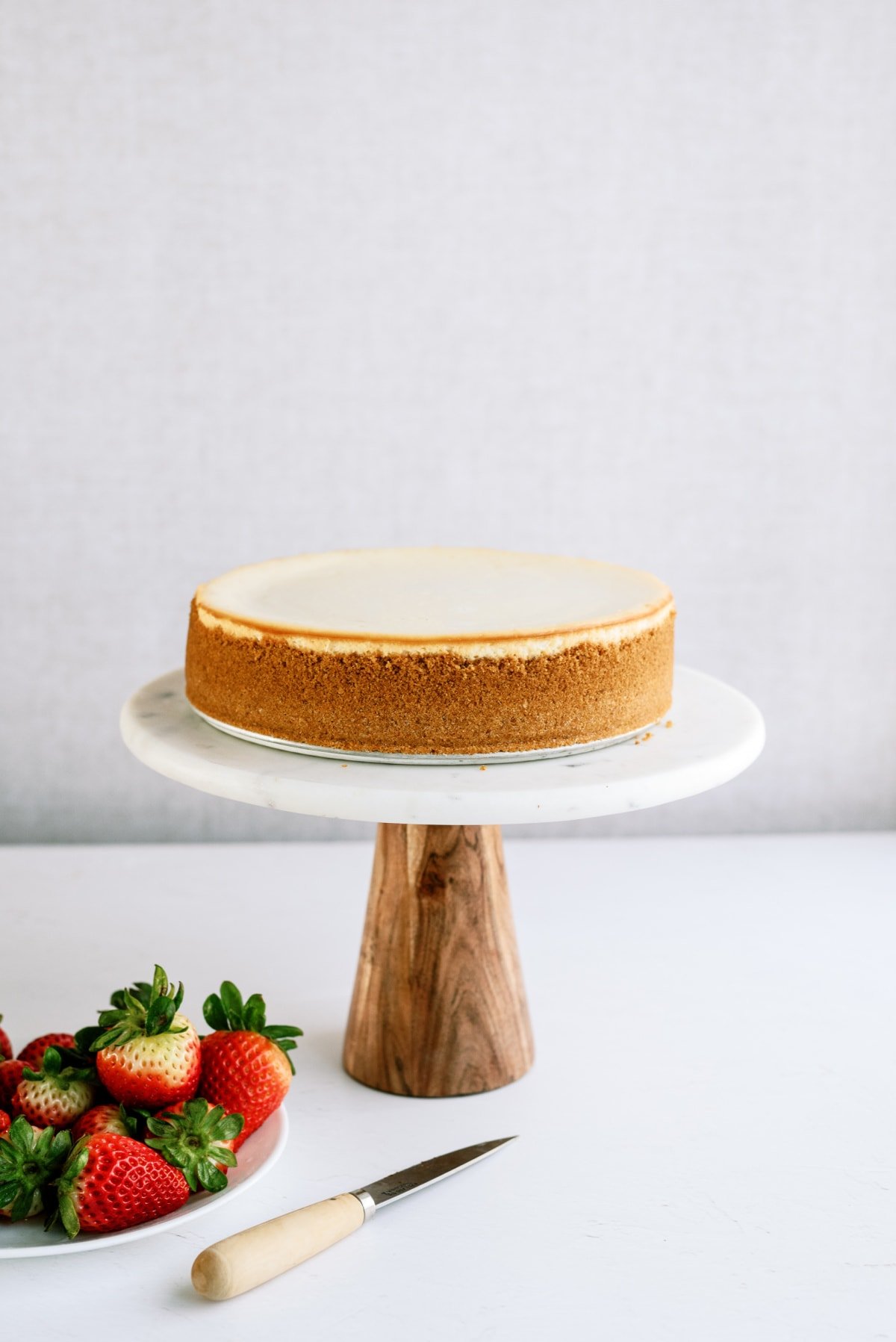 cheesecake on stand with plate of strawberries