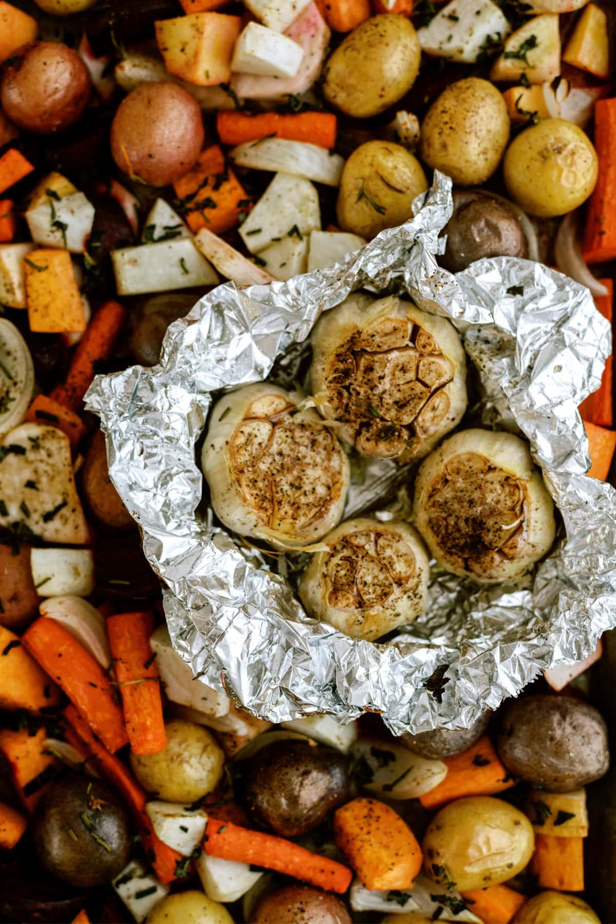cooked roasted root vegetables on sheet pan with garlic in foil