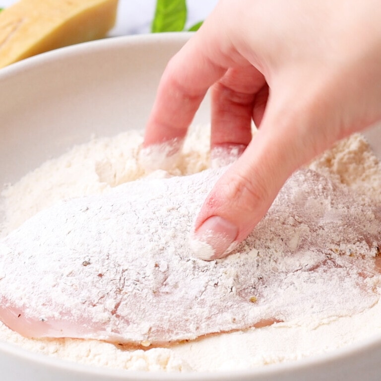 Woman's hand flouring chicken breast
