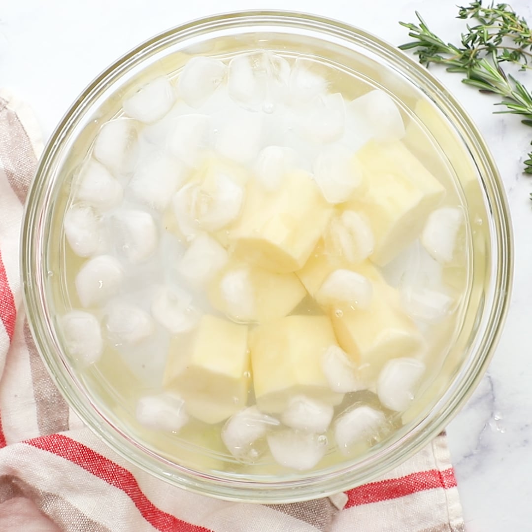 raw potatoes soaking in glass bowl of ice water