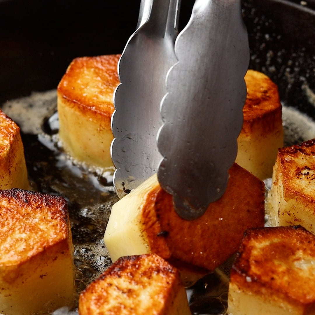 tongs turning over FONDANT POTATOES in cast iron skillet
