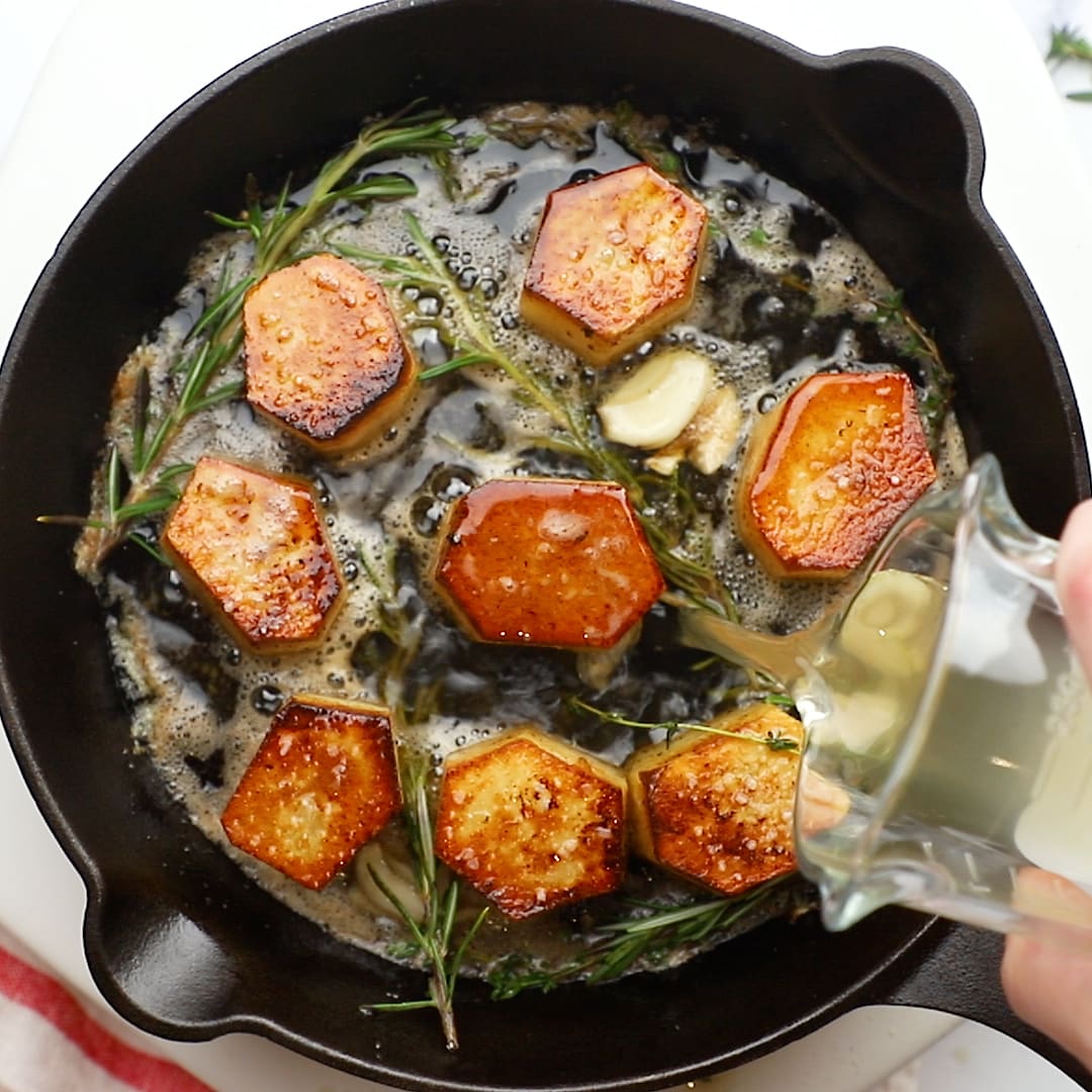 pouring broth over FONDANT POTATOES in cast iron skillet