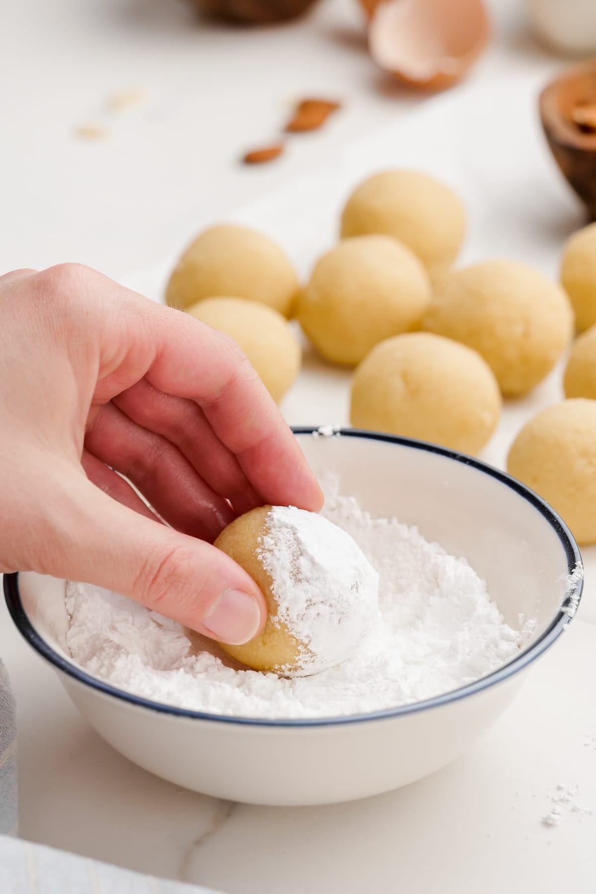 woman's hand dipping amaretti cookies dough ball into powdered sugar