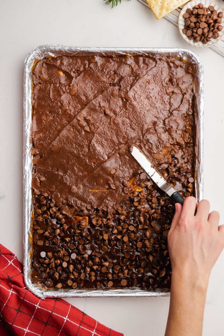 woman's hand spreading chocolate onto christmas crack on baking sheet