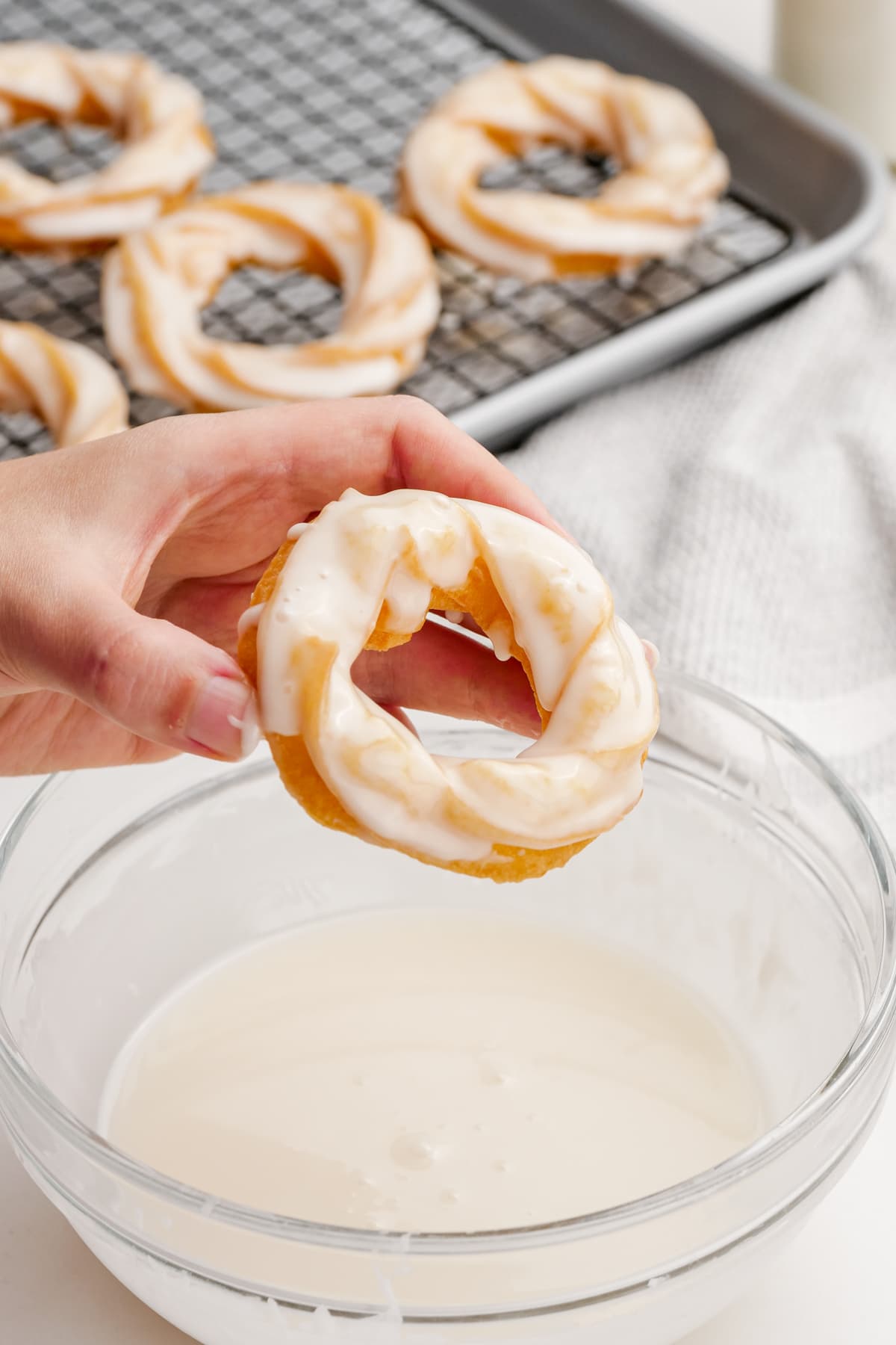woman's hand dipping french crullers in glaze