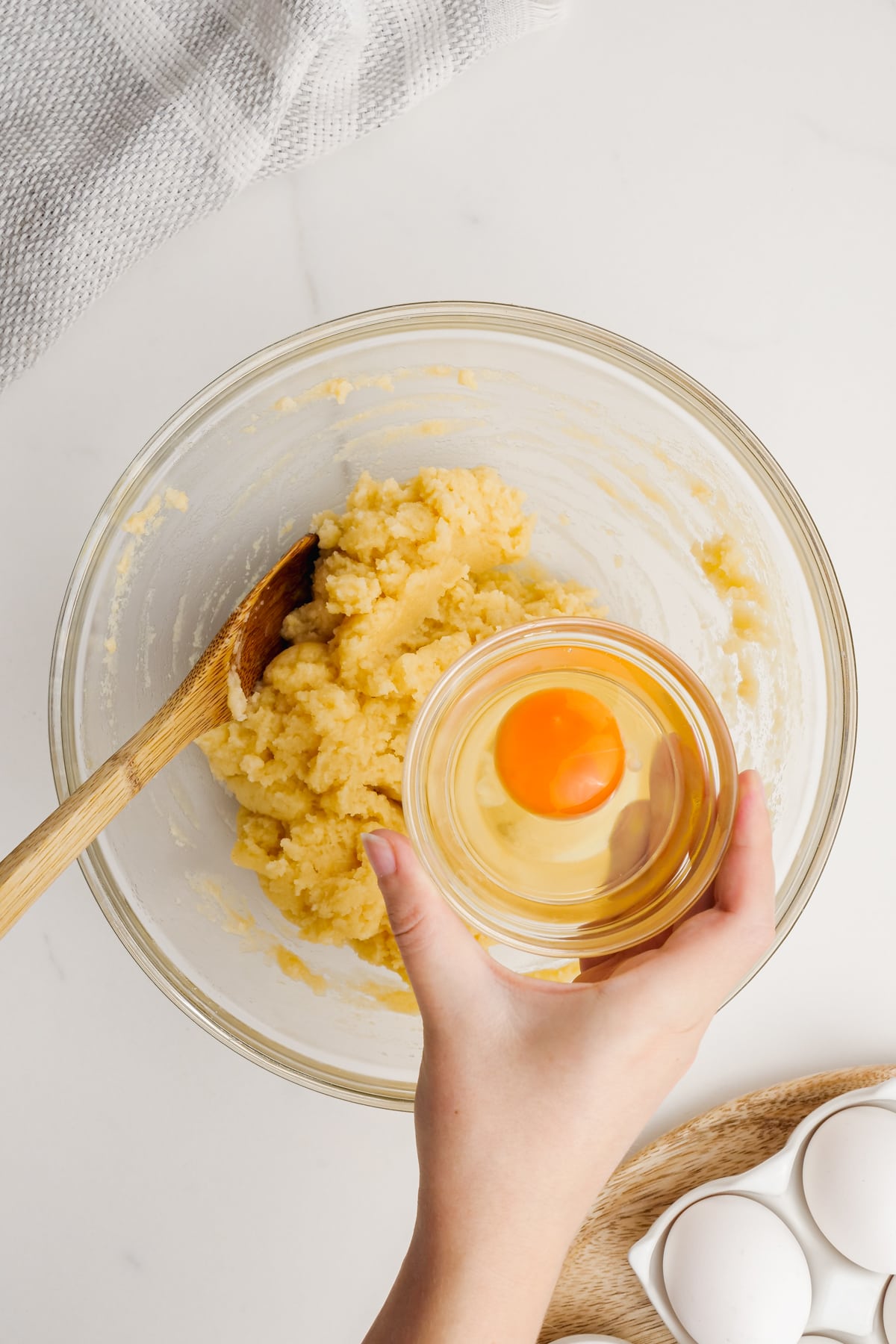 woman's hand putting egg in bowl of french cruller dough