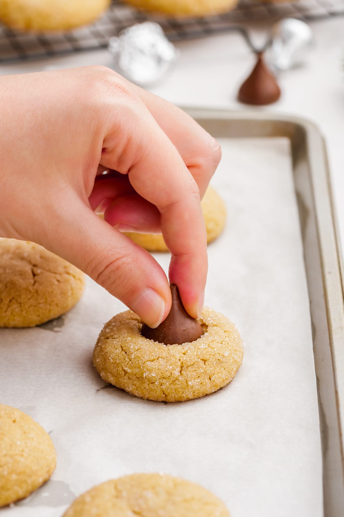 woman's hand placing hershey's kiss into peanut butter blossoms cookie