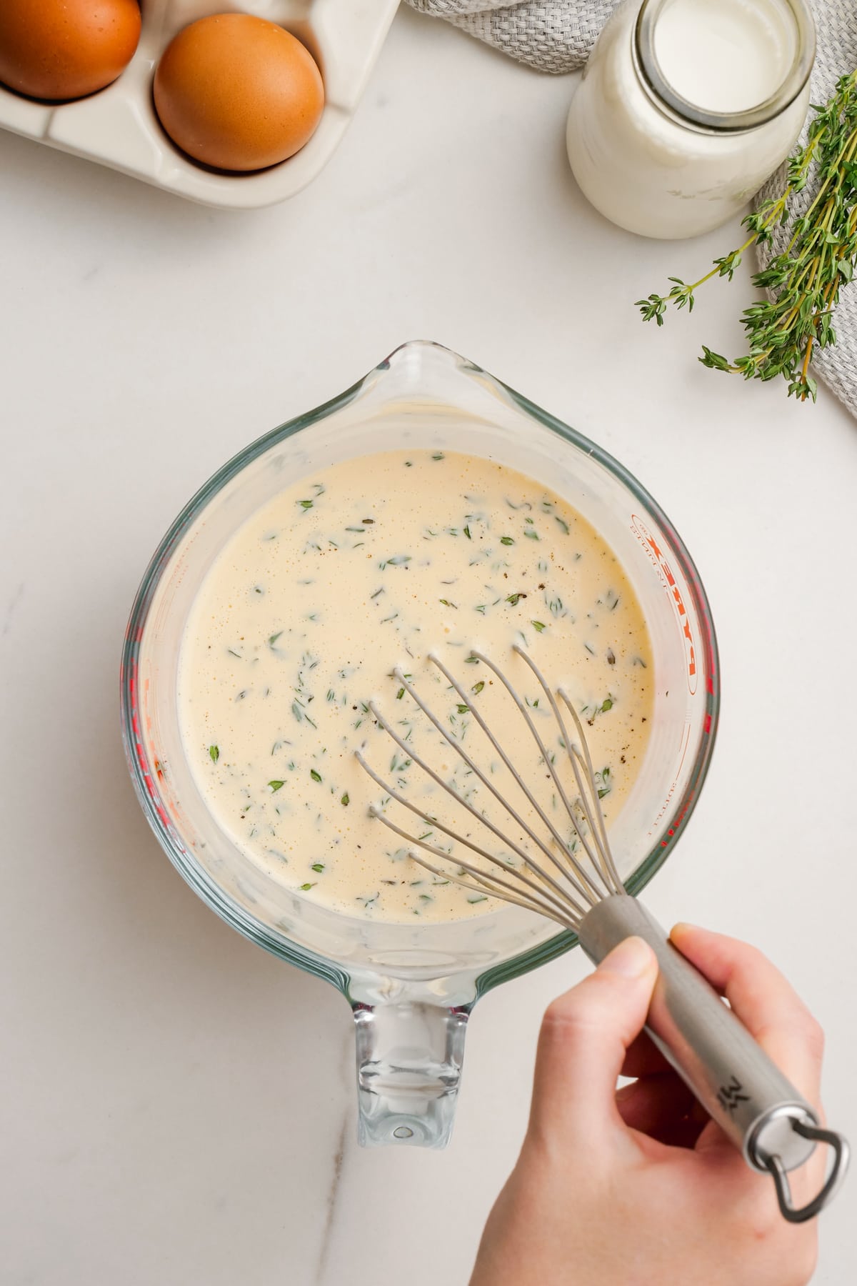 woman's hand whisking quiche lorraine ingredients in measuring cup