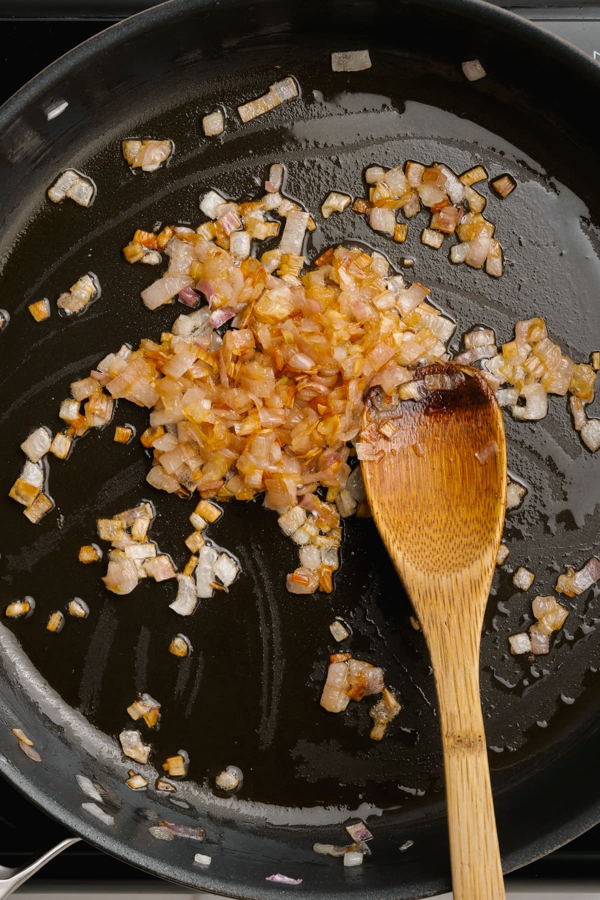 cooked diced shallot in skillet with wooden spoon