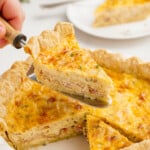 woman's hand scooping piece of quiche lorraine out of pie pan