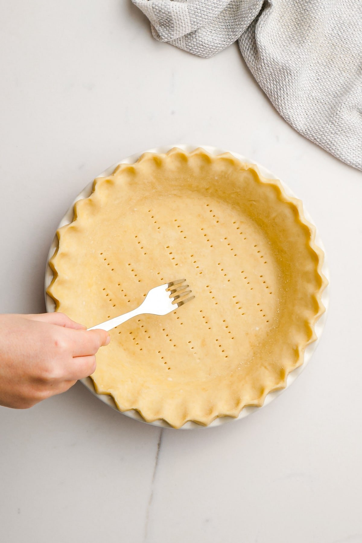 woman's hand piercing raw pie crust with fork