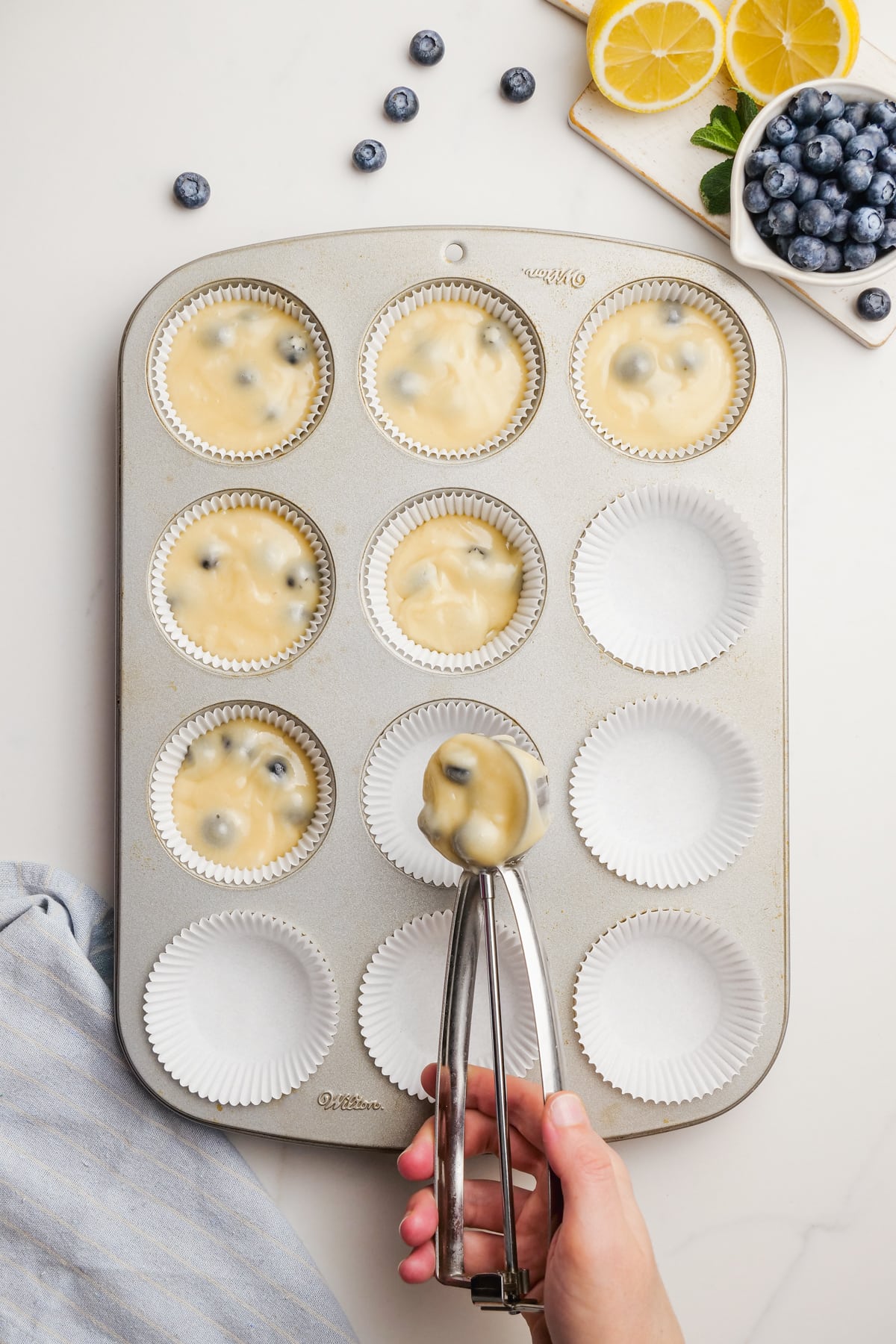 woman's hand scooping blueberry-muffins batter into cupcake pan