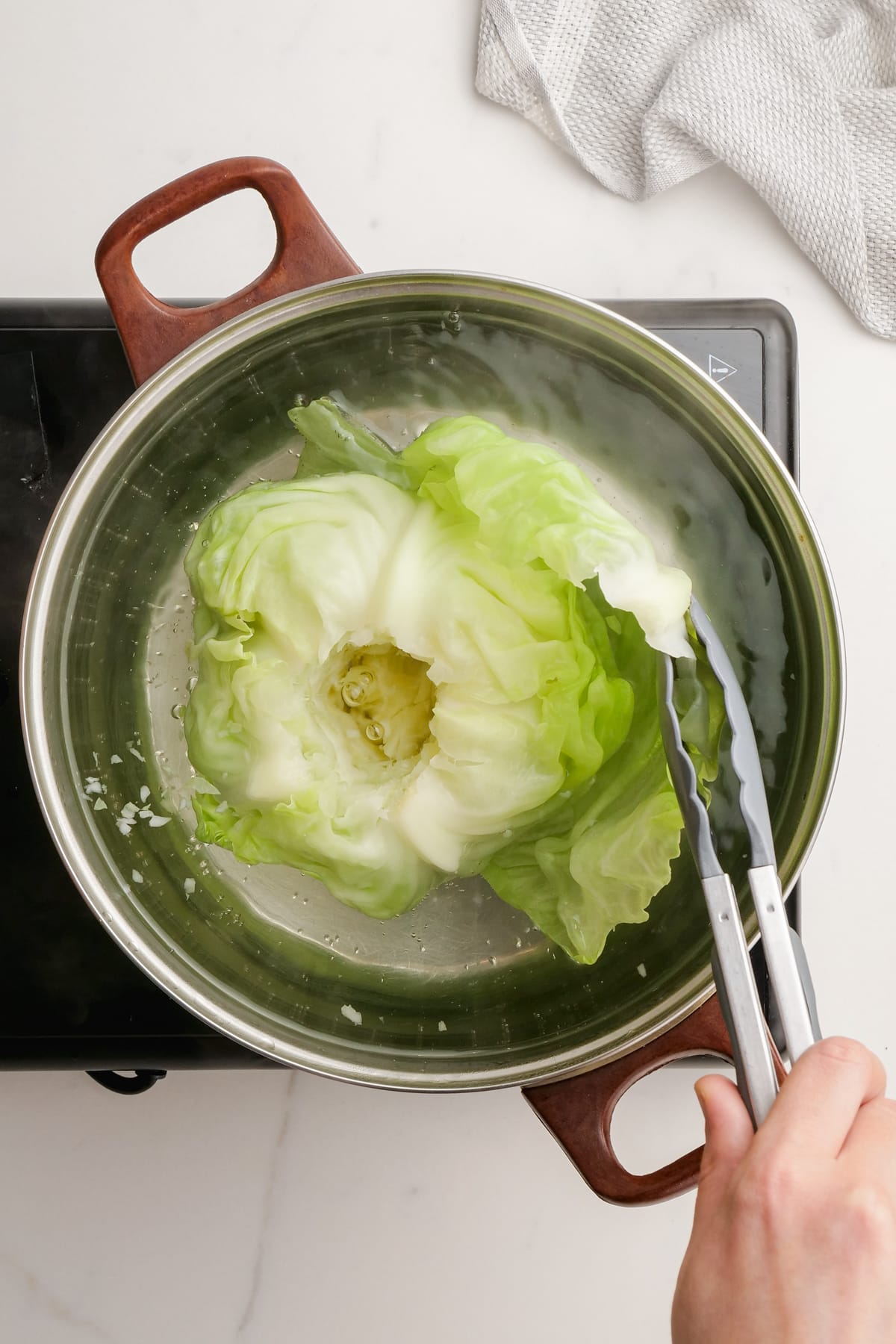 boiling cabbage in pot and pulling off loose leaves with tongs